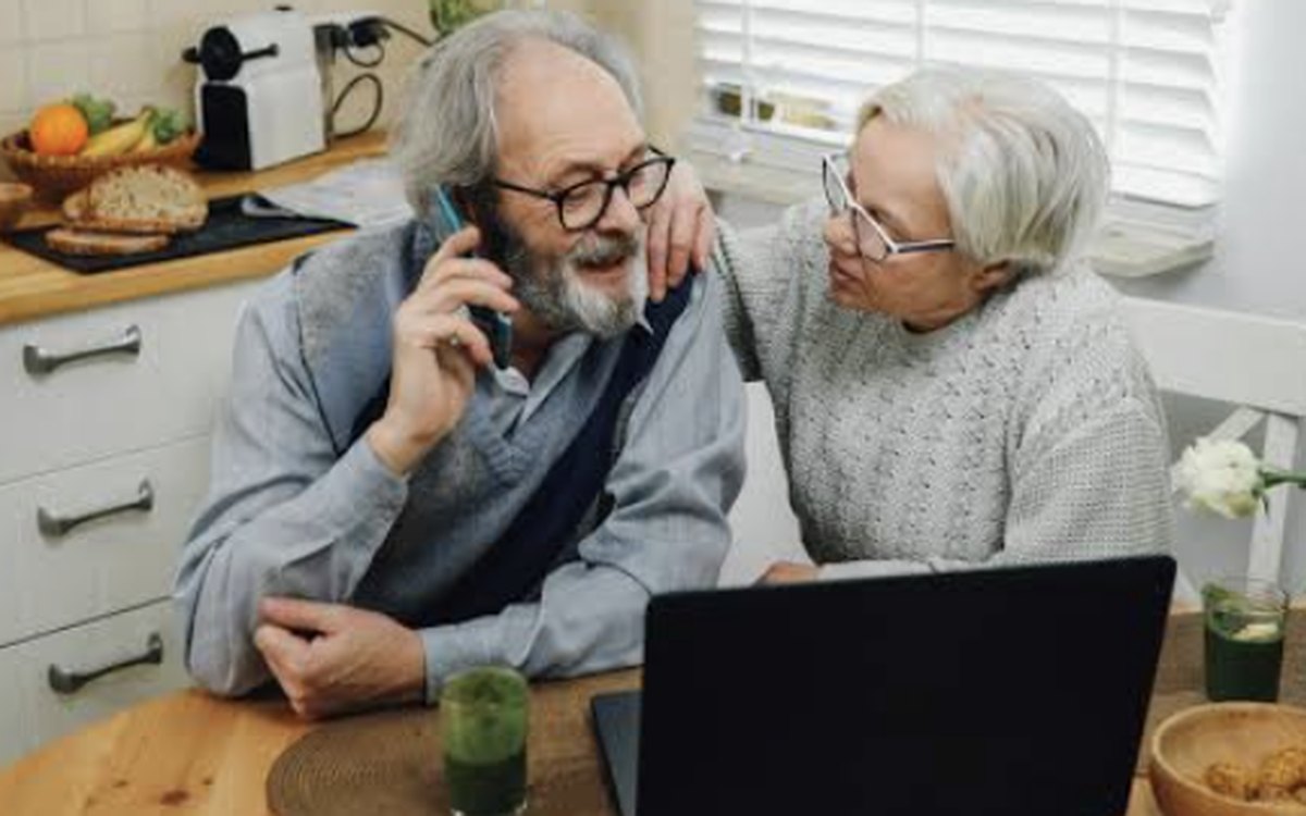A couple at their kitchen table at home, on the phone with a laptop open